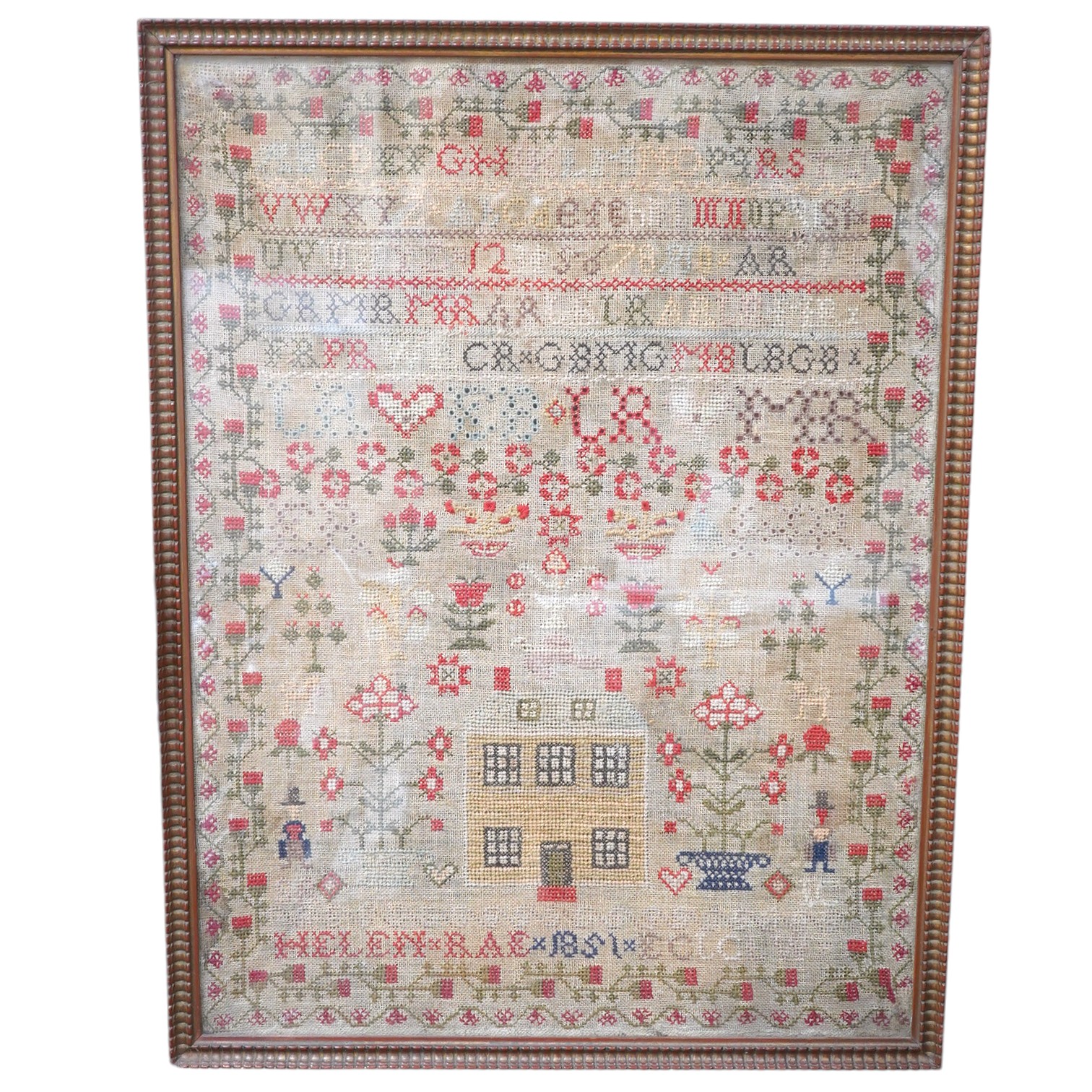 A large framed cross stitch sampler, by Helen Rae, dated 1851, worked mostly in red and green, with an ornate floral border around alphabet letters and numerals, large button hole letters and motifs, with a large central